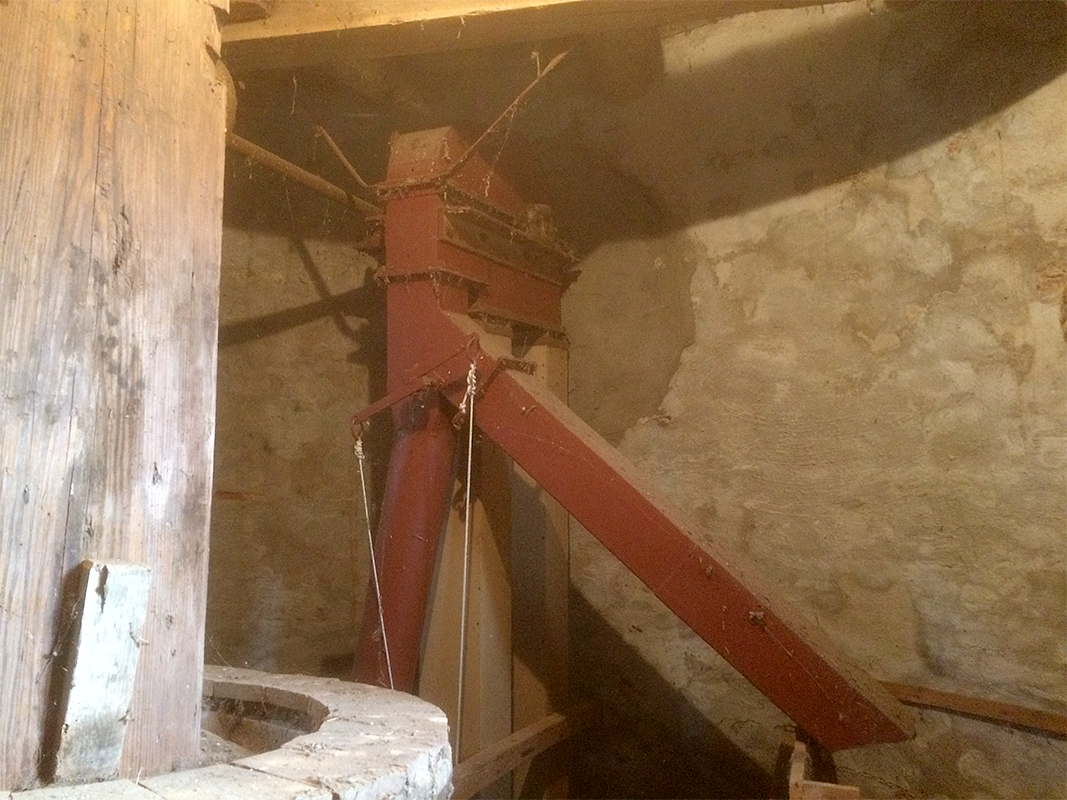 16, Molen 00872 Braamse Molen / Koenders Möl (Braamt), Fabian Gerritsen (25-11-2017)De elevatorkop met pijpen naar de silo, menger, en buil. Goed is te zien, dat de elevator op de plek zit waar het luiwerk vroeger zat, dit luiwerk is met de restauratie/modernisering van 1963 verwijderd, alleen de luitafel zit nog om de koningspil. De sleuf waar het gaffelwiel doorheen liep, is later dicht gesmeerd. | Database Nederlandse molens