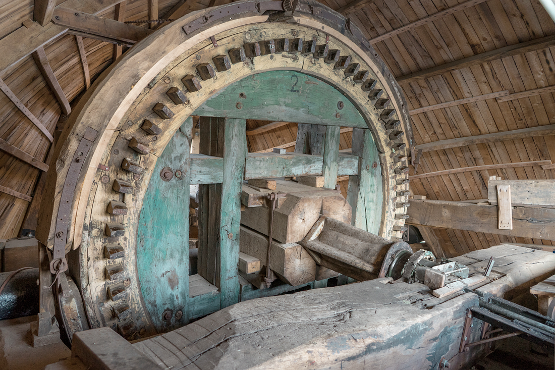 12, Molen 00276 De Zuidmolen (Groesbeek), Marcel van Nies (8-4-2017)Bovenwiel, met een doorboorde as. Rechtsonder in beeld de stang die door de as steekt, om de Ten Havekleppen te regelen. Achter, boven de penbalk, de vangbalk. | Database Nederlandse molens