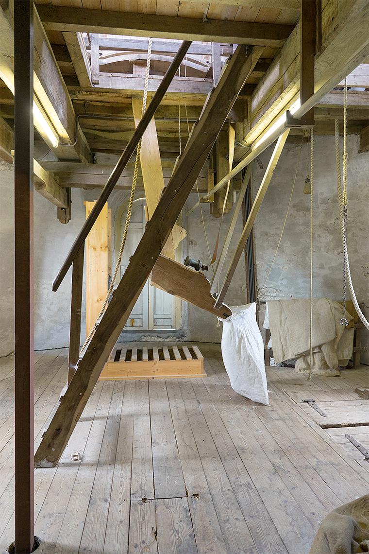 10, Molen 02781 Windlust (Nederweert-Roeven), Marcel van Nies (25-4-2018)Links op de voorgrond de vierkante ijzeren as voor de aandrijving van de oliemolen. Op de achtergrond een houten 'kast' waarin de heien op-en-neer bewegen en waarin de twee spaken van de wentelas ronddraaien. | Database Nederlandse molens