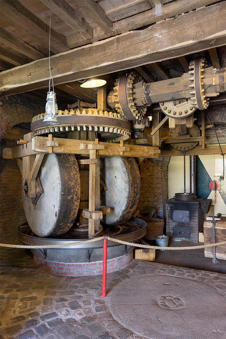 11, Molen 02781 Windlust (Nederweert-Roeven), Marcel van Nies (25-4-2018)De koningstrijker met afloper is neergelaten en voert het geplette goed naar afloopbak, waar het in de houten bak rechtsonder/naast de kollergang valt. Daaruit wordt het meel in de vuisterring geschept. | Database Nederlandse molens