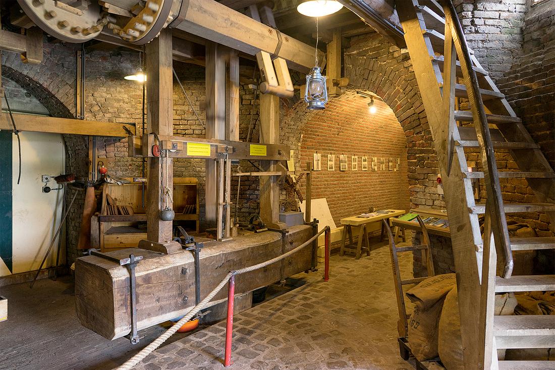 12, Molen 02781 Windlust (Nederweert-Roeven), Marcel van Nies (25-4-2018)Het oranje pannetje links- en het zwarte pannetje rechtsonder de slagbank vangen de olie -het hoofdprodukt- op. De wentelas heeft twee spaken. Op de foto valt net de slaghei omlaag. | Database Nederlandse molens