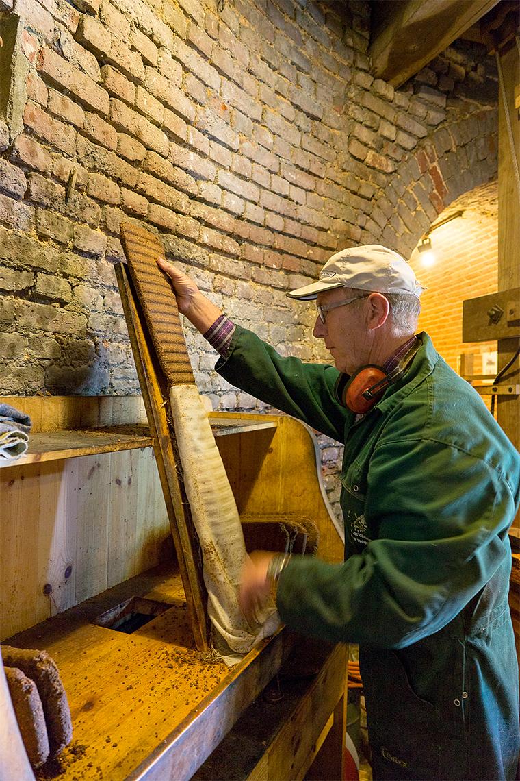 21, Molen 02781 Windlust (Nederweert-Roeven), Marcel van Nies (25-4-2018)Tot slot wordt de overgebleven inhoud, de koek -een bijprodukt- uit de bulen gehaald op de strooptafel. Op de kaak wordt een buul van de koek gestroopt. De bulen worden herbruikt. | Database Nederlandse molens