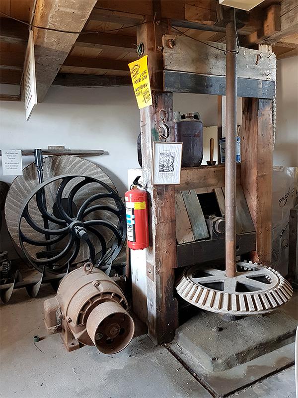 8, Molen 01658 Nooit Gedacht (Eindewege ('s Heer Arendskerke)), Pieter Zuijkerbuijk (5-7-2019)De vliegwielen en wat andere materialen van de voormalige mechanische aandrijving, helaas hebben de Heemaf Elektromotor en de aanzetweerstand geen geschiedenis met de molen. De fraaie haakse overbrenging incl de assen en het rondsel is ook bewaard. | Database Nederlandse molens