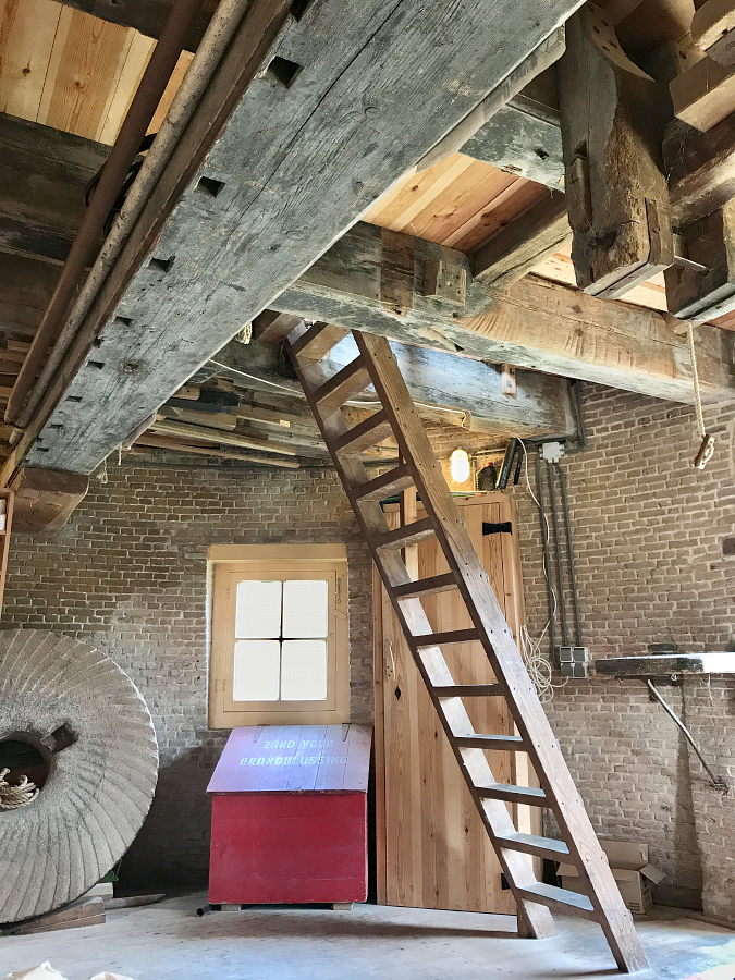 9, Molen 01537 De Drie Lelies (Maasland), Toby de Kok (21-9-2017)De maalzolder met op de achtergrond een molensteen, een bak waar vroeger zand in lag voor brandblussing en een zakkenbankje naast de hoofdingang op het oosten. De draagbalk is een oude houten roede. | Database Nederlandse molens